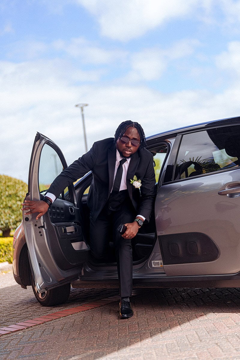 Stylish man in black suit stepping out of a luxury car for a formal occasion.