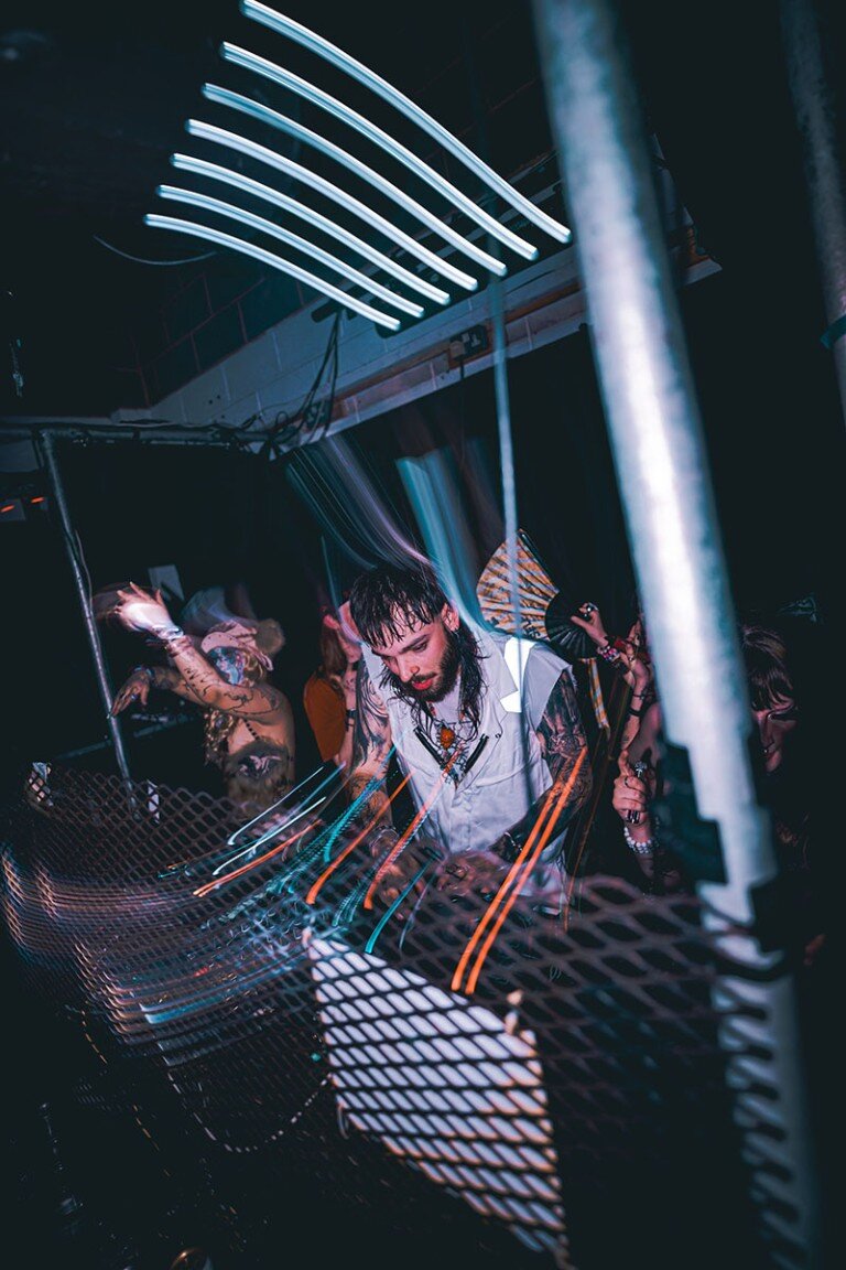 Vibrant DJ performing at a nightclub with colourful light effects and a lively atmosphere.