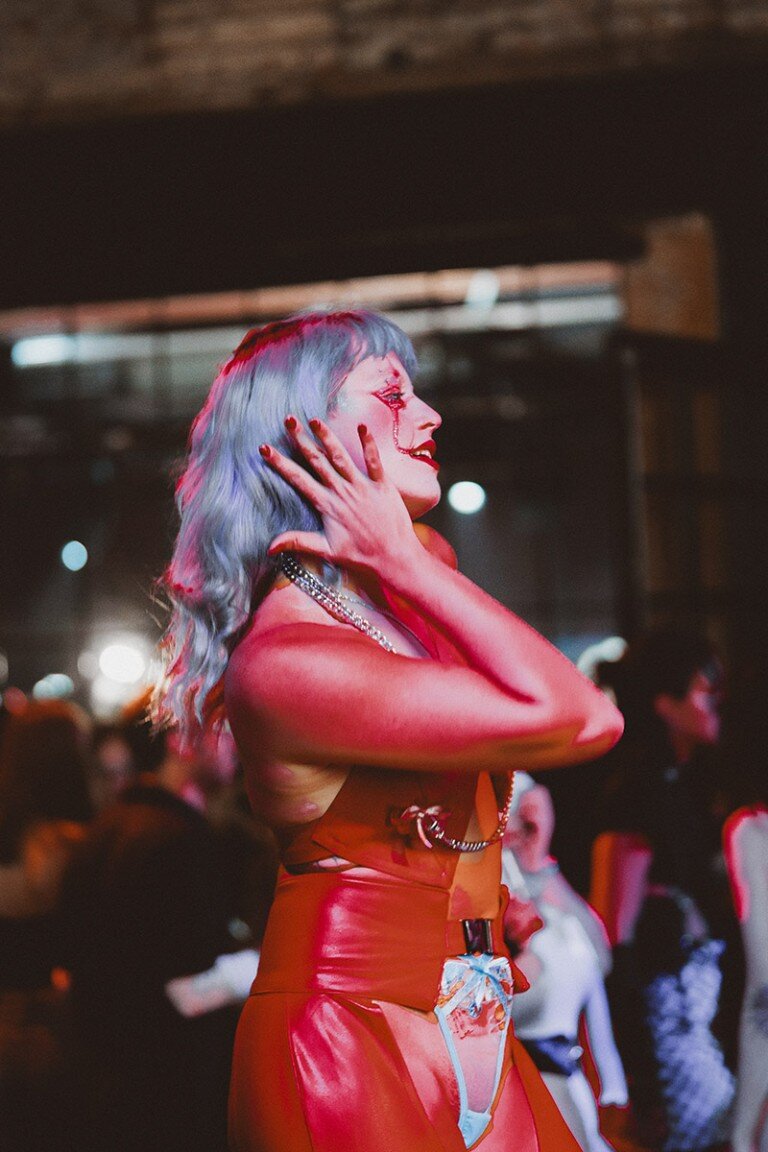 Vibrant performer with colourful hair and dramatic makeup performs at nightlife event.