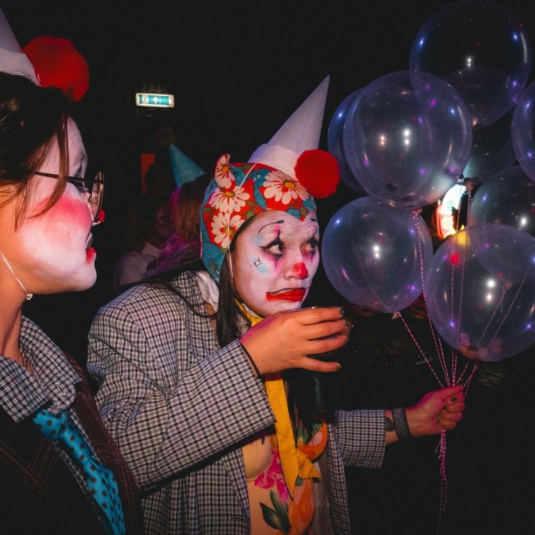 Vivid clown and party costumes with balloons at a celebration or event. Bright colours and festive atmosphere with clown makeup and hats.