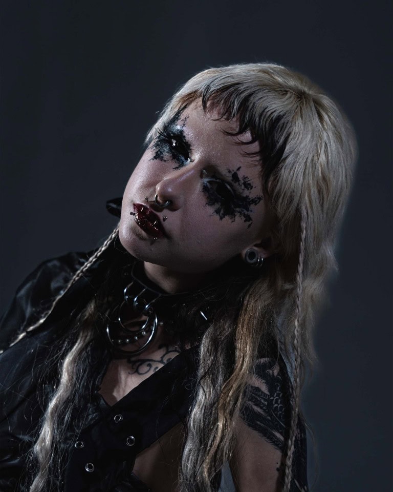 Close-up of a person with goth-inspired makeup, piercings, and dyed hair, showcasing alternative fashion style.