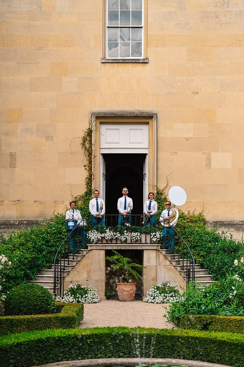 Elegant jazz band performing on a balcony outside a historic building with lush garden surroundings.