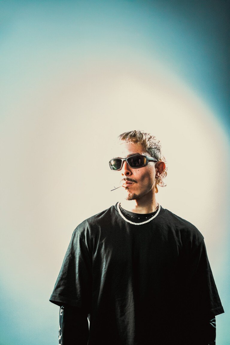 Stylish young man wearing sunglasses and jewelry against a colourful gradient background.