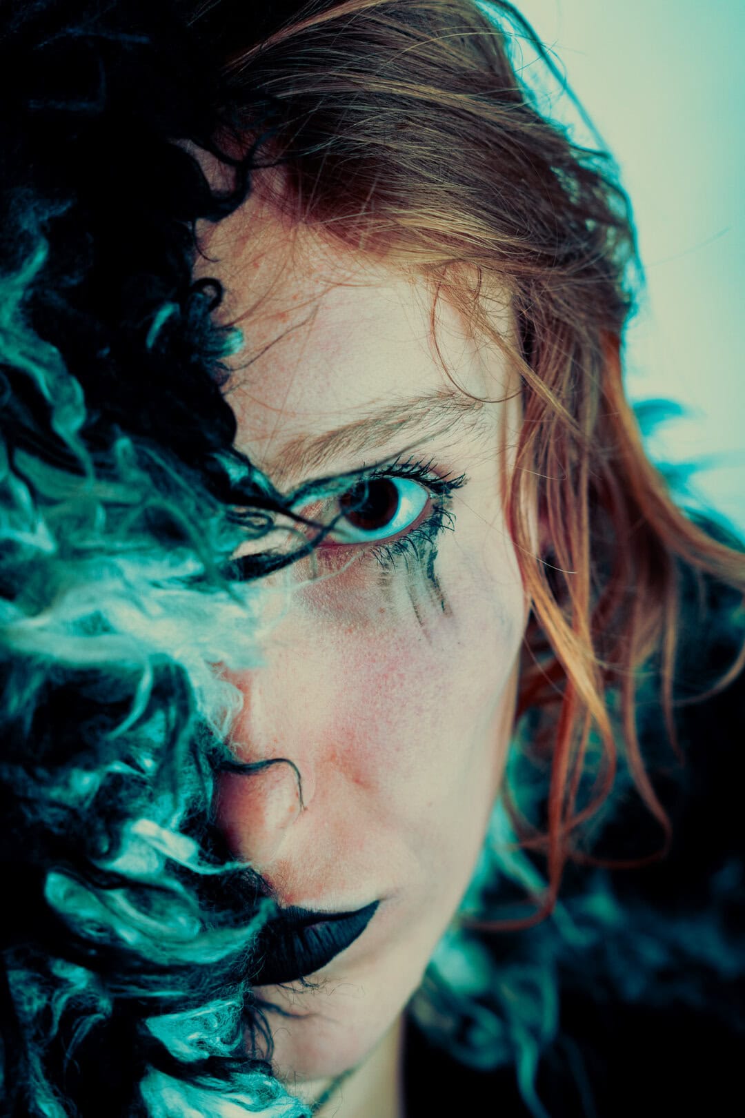 Vibrant portrait of a woman with striking eye makeup and piercing blue eyes, surrounded by contrasting black curly hair.