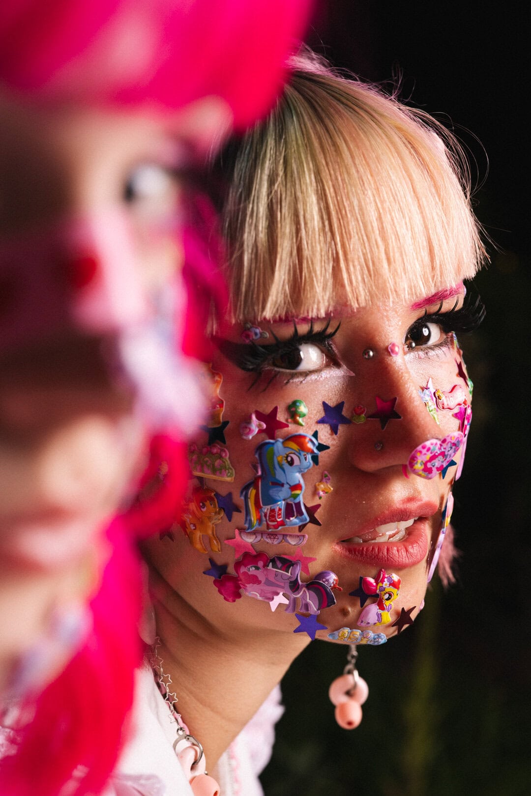 Colourful face decorated with My Little Pony stickers and elaborate makeup, showcasing creative festival or costume makeup.