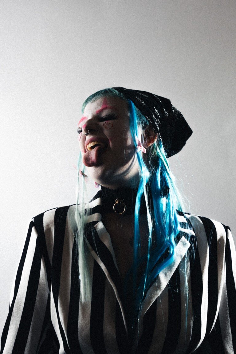 Vibrant edgy woman with colourful hair, piercings, and striped outfit, expressing attitude and individuality.