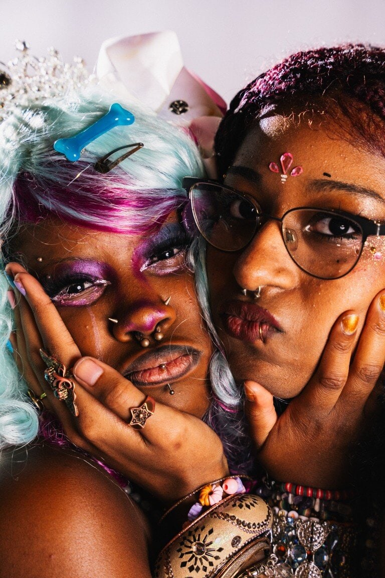 Vibrant portrait of two women with colourful hair, bold makeup, and striking accessories, expressing individuality and creativity.