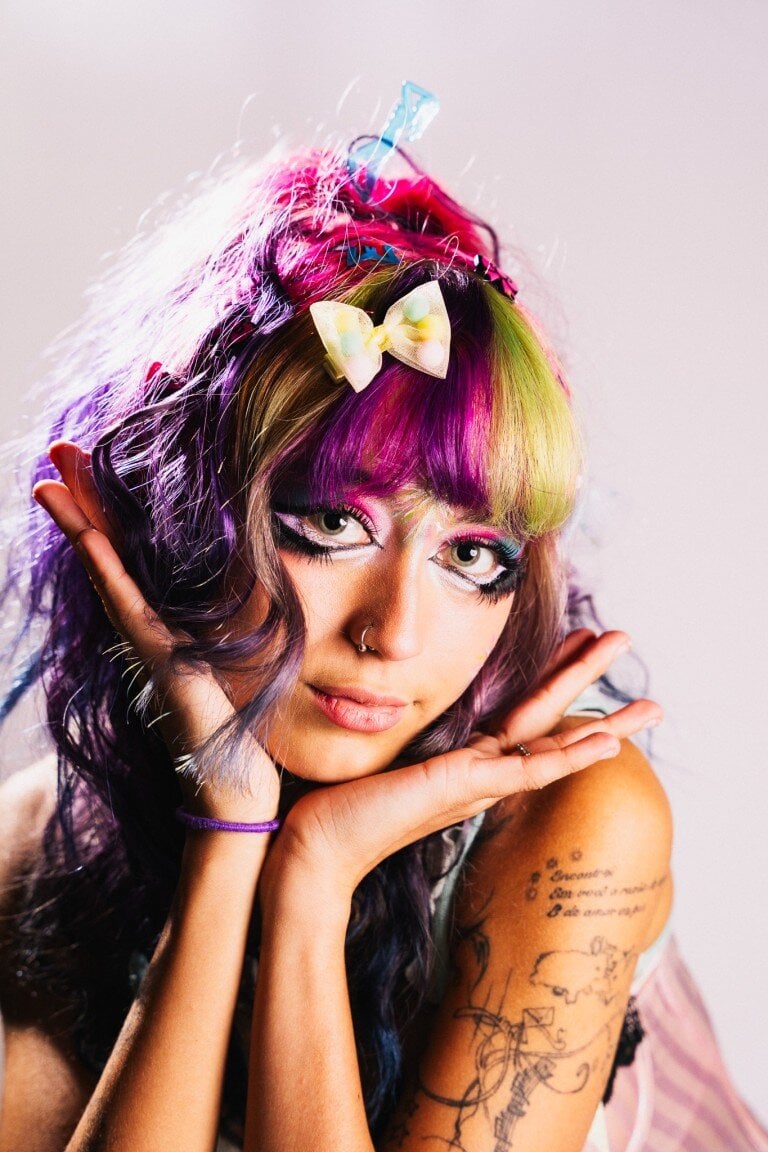 Bright colorful hairstyle with pastel hair bows, vibrant makeup, and tattoos, showcasing expressive fashion and creative styling.