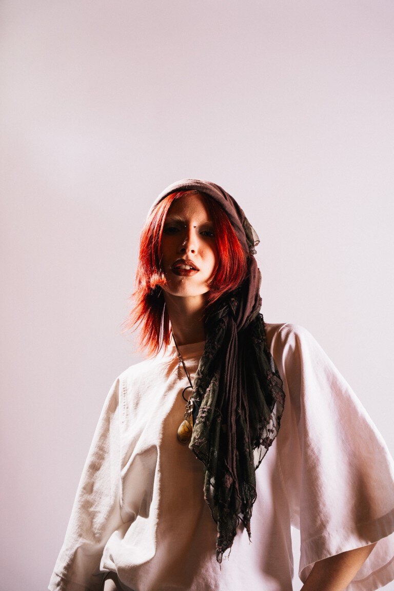 Vibrant red-haired woman with a black lace headscarf and beige clothing, fashion-forward model.