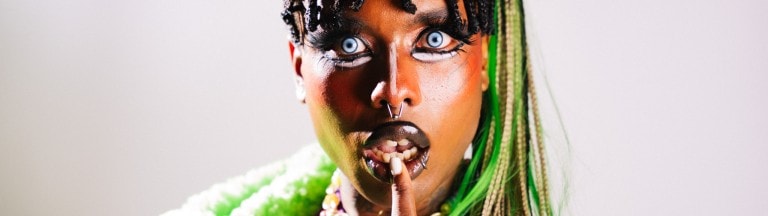 Vibrant portrait of a woman with bold makeup and colourful accessories, expressive with striking blue eyes.