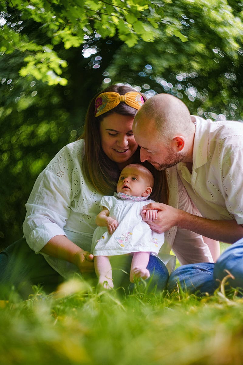 Warm family enjoying outdoor time with baby, surrounded by green foliage in a park setting.