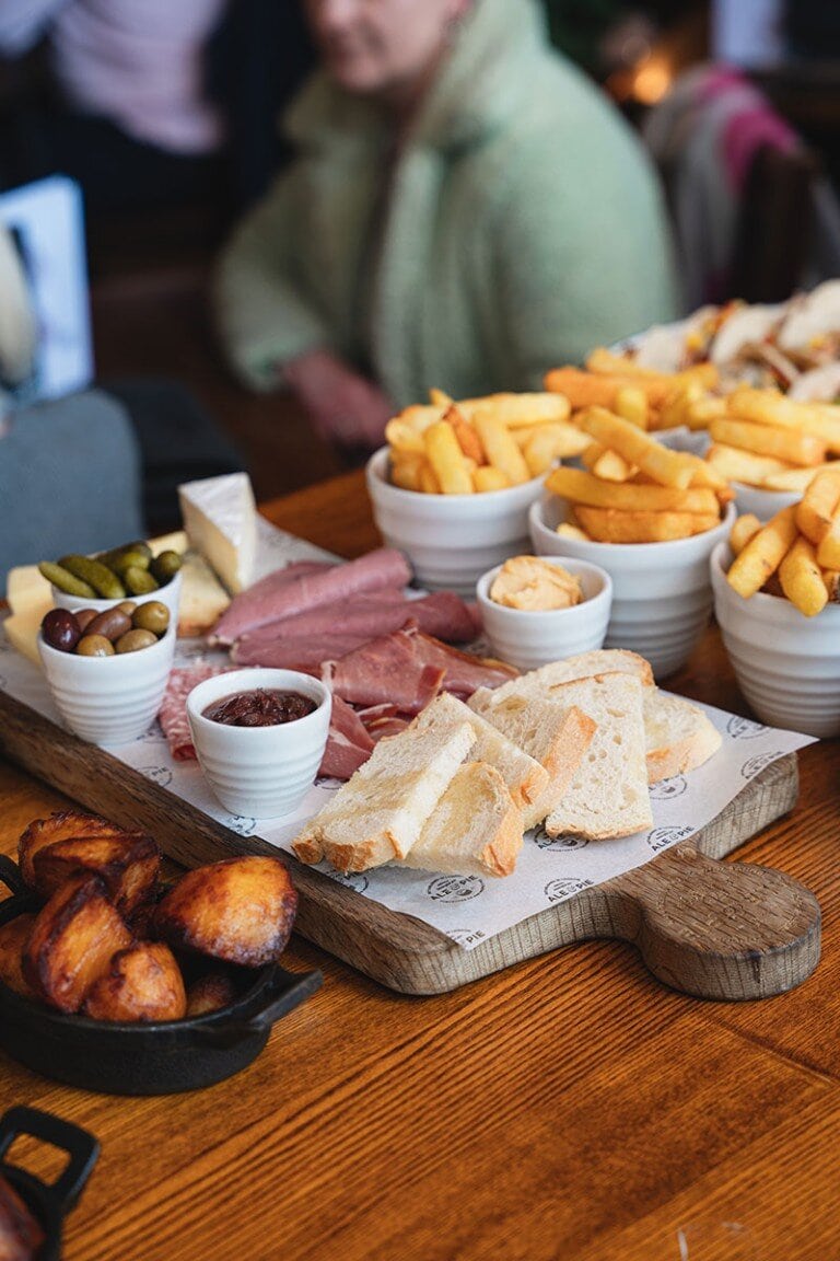 Crispy fried potatoes and assorted cold cuts on wooden serving platter, pub dining scene.