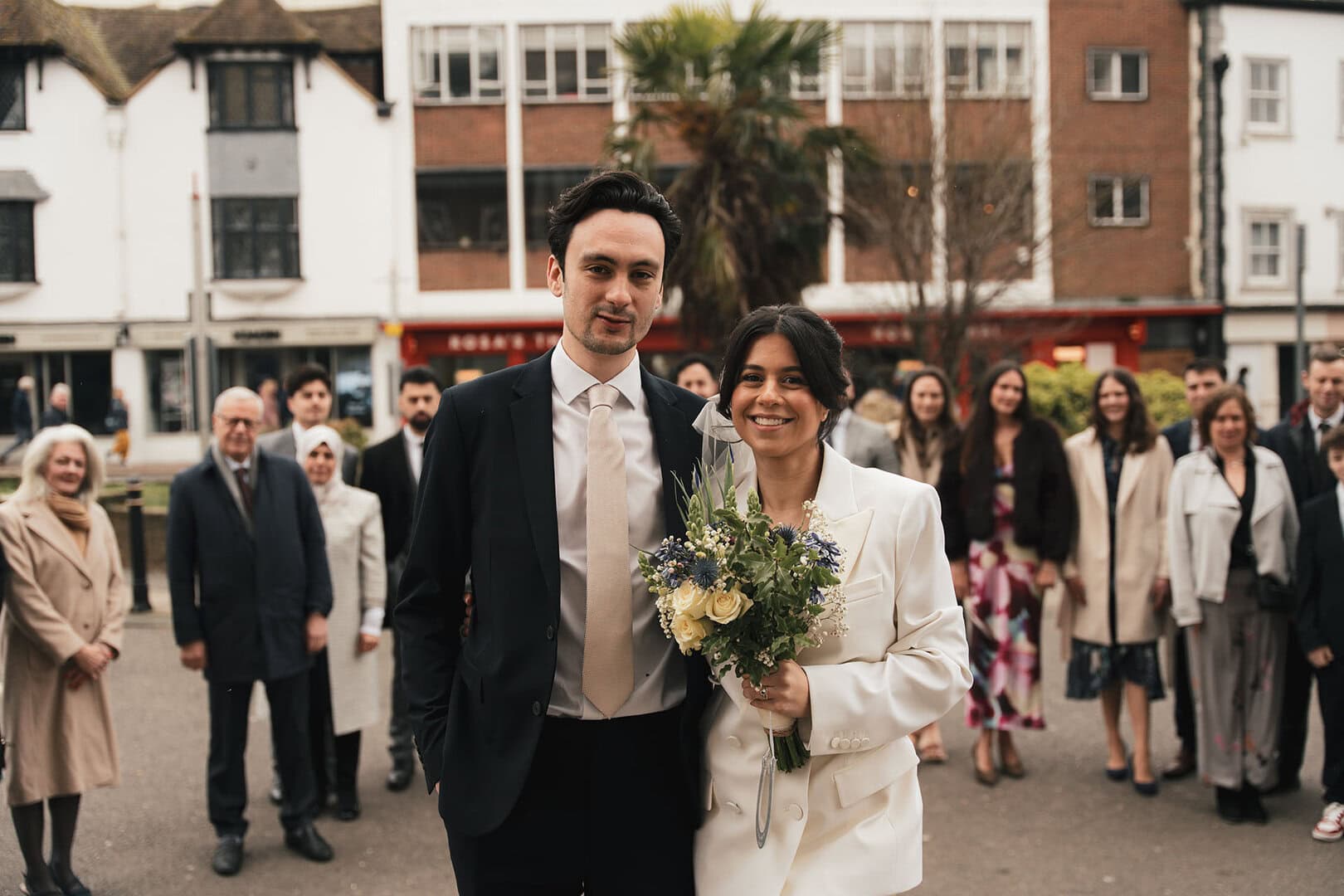 Beautiful wedding celebration outdoors with smiling bride and groom, surrounded by friends and family.