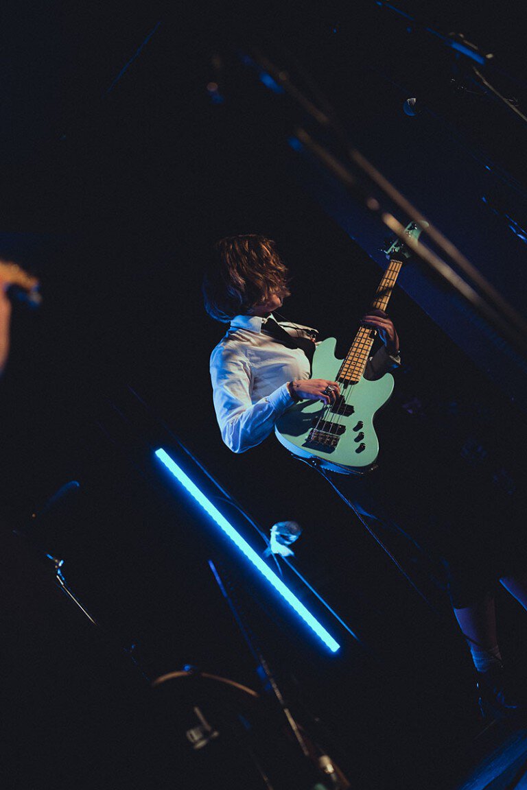 Guitarist performing on stage with blue lighting at a music concert.