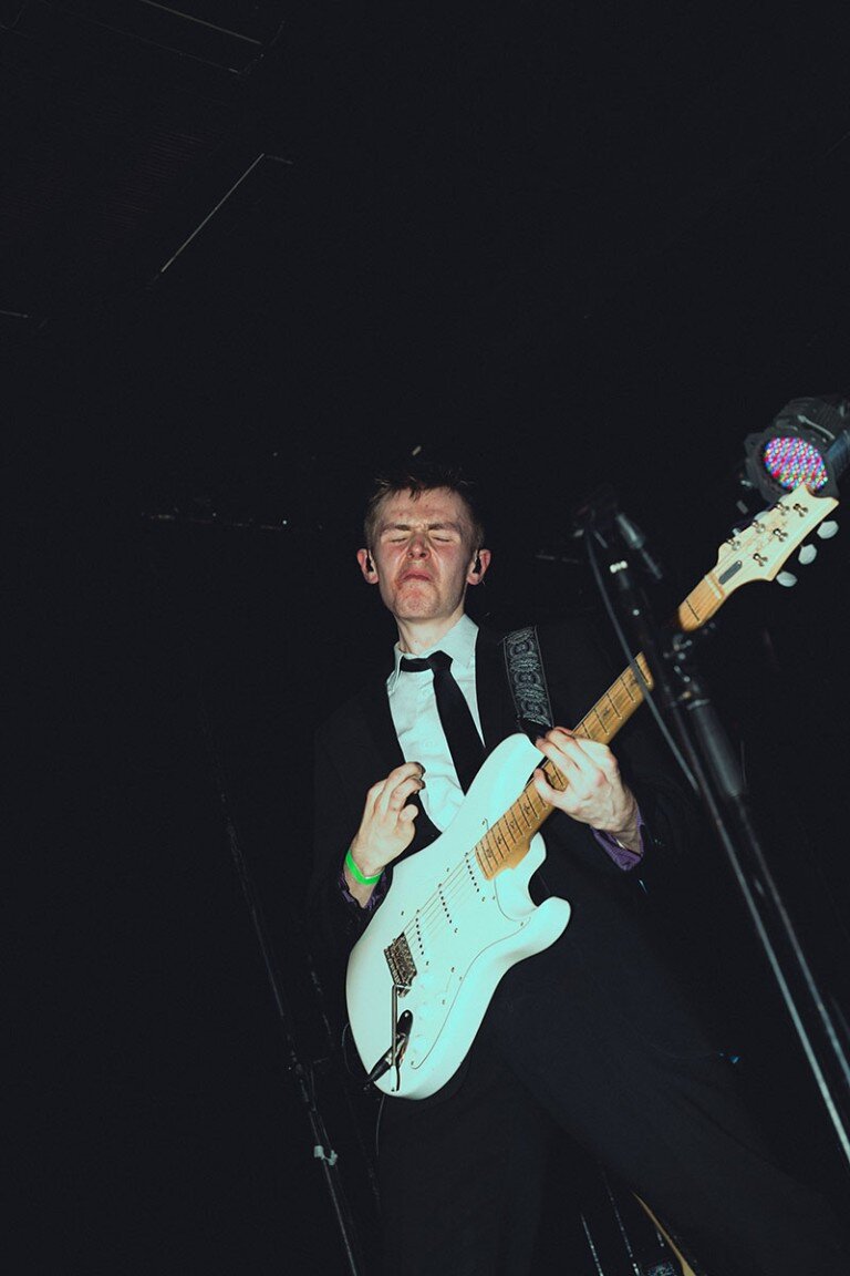 Guitarist performing passionately on stage with intense facial expression at a live music event.