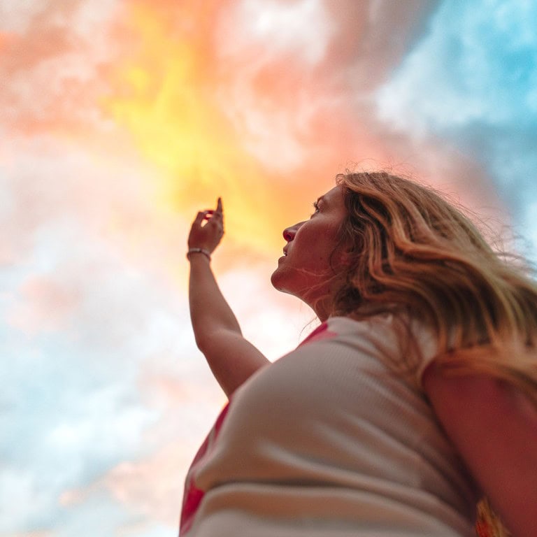 Vibrant sunset sky with a woman reaching upwards, capturing colourful clouds and serene atmosphere.