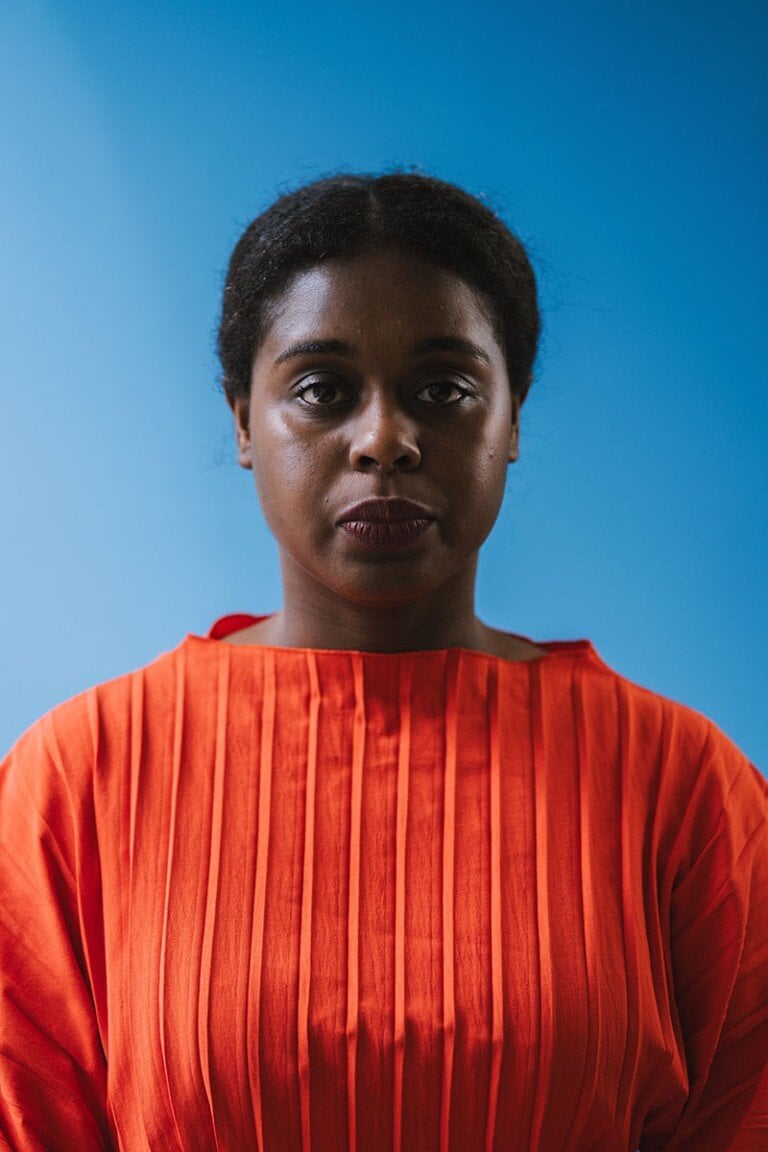 Black woman wearing red pleated dress against blue background.