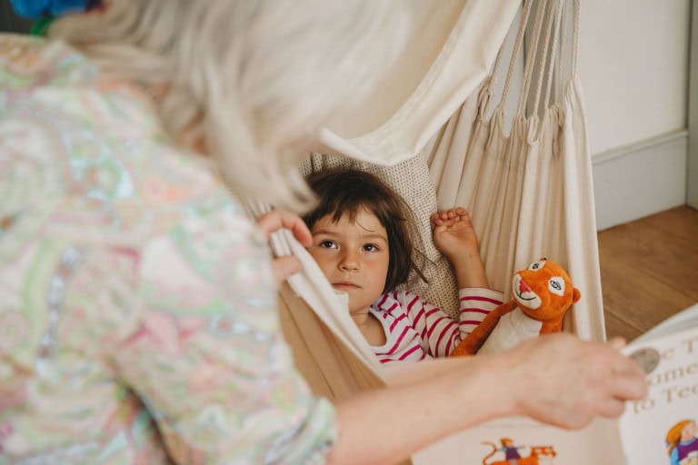 Cute young girl lying in a hammock with a stuffed tiger toy, enjoying storytime at home.