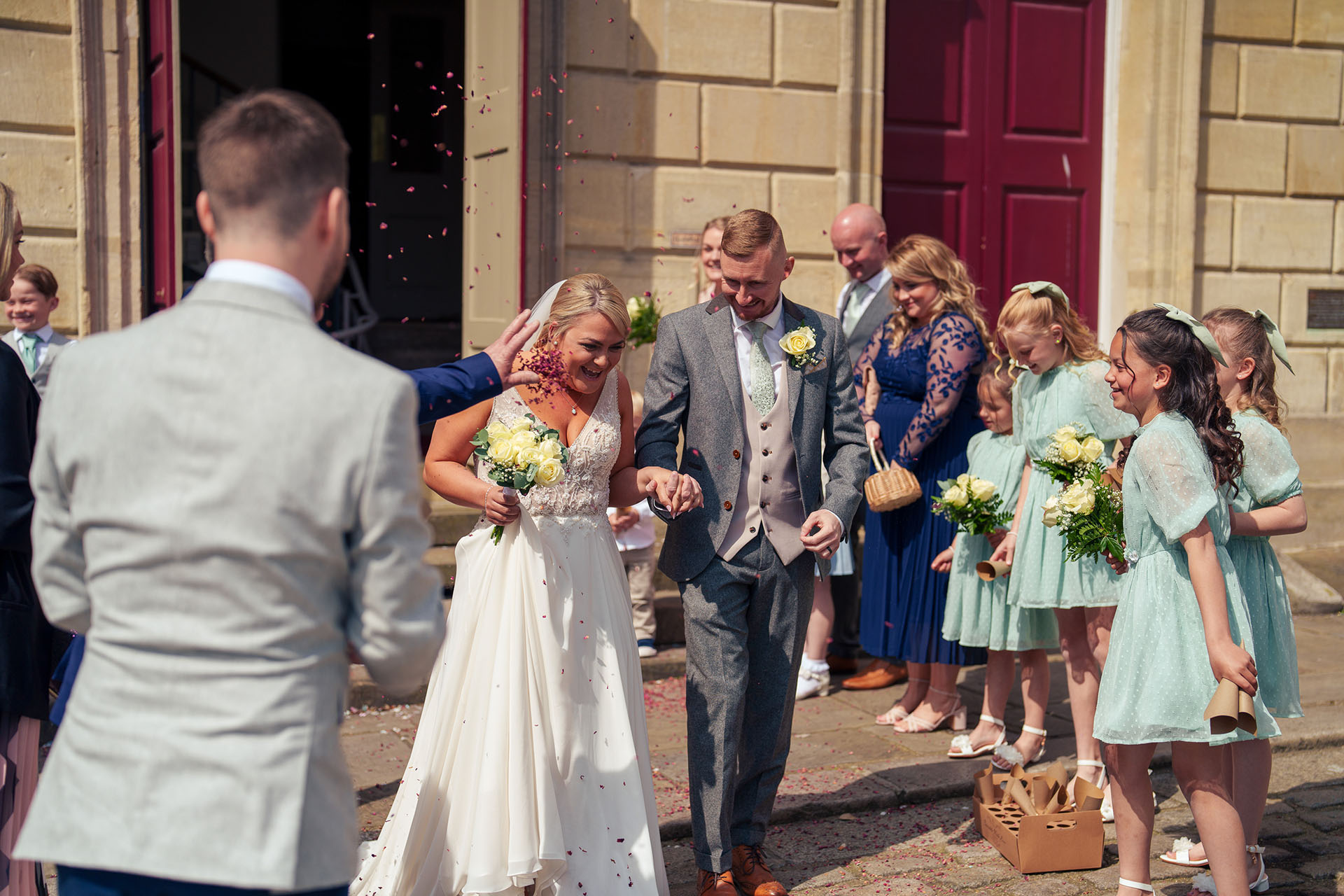 Confetti throwing at wedding outside church, bride and groom celebrating with guests, wedding day joy and happiness, outdoor wedding celebration, LemonLens.
