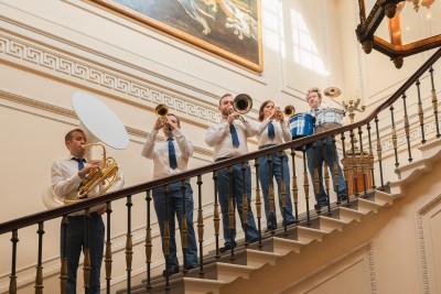 Band performing jazz on staircase in elegant historic building, musical instruments, stylish formal attire, sophisticated ambiance, live performance, classic interior design.