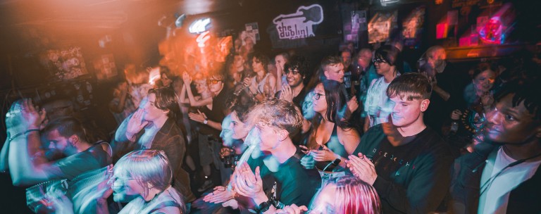 Bright crowd enjoying live music at a vibrant nightclub with colourful lighting effects.