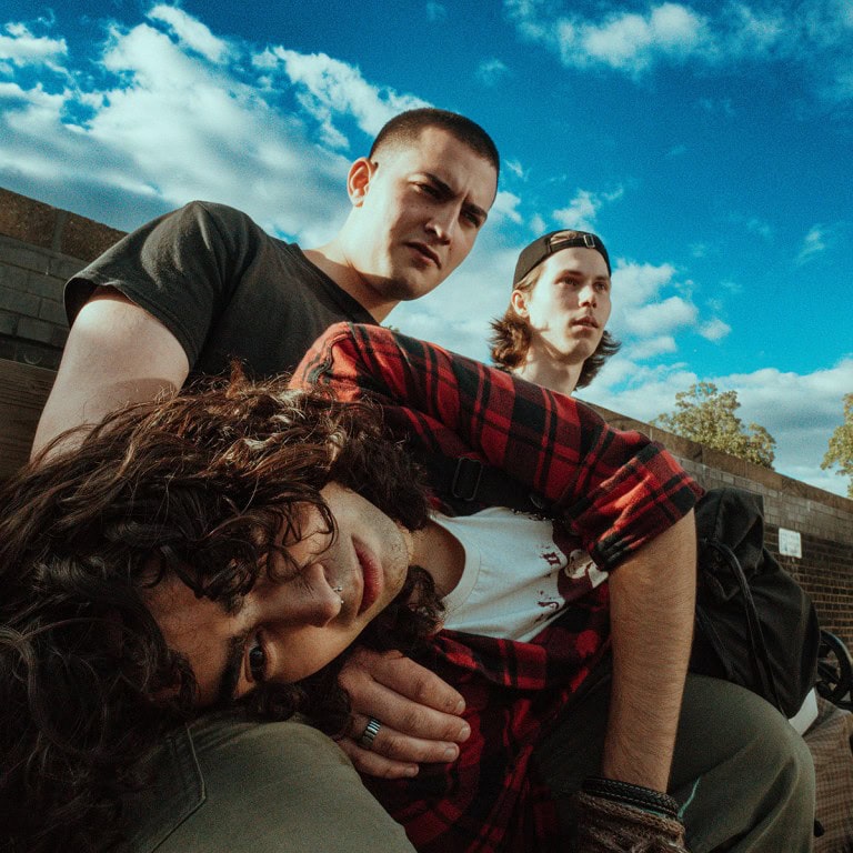 Friends sitting outdoors on a sunny day, looking serious and contemplative, urban background, casual streetwear style, vibrant sky.