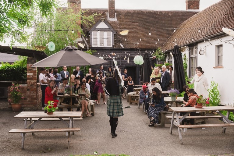 People gathered at an outdoor courtyard event with decorations and string lights in a rustic setting.