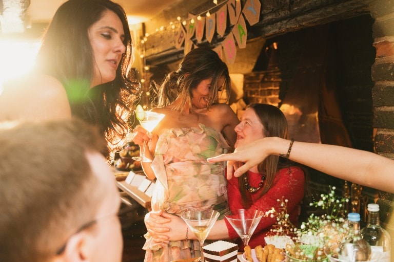 Celebration of friends enjoying a birthday party in a cosy, warmly lit home with drinks and snacks.