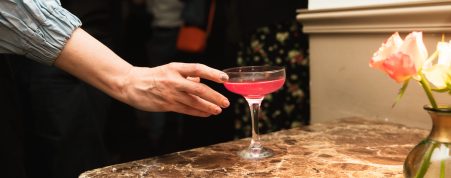 Pink cocktail in a coupe glass at a bar or event venue.
