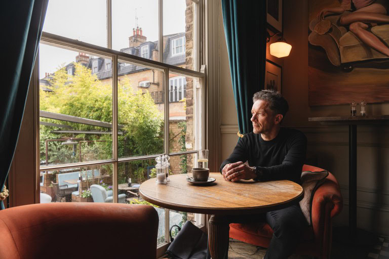 Man sitting by a window with coffee in a cosy café setting, enjoying a peaceful moment.