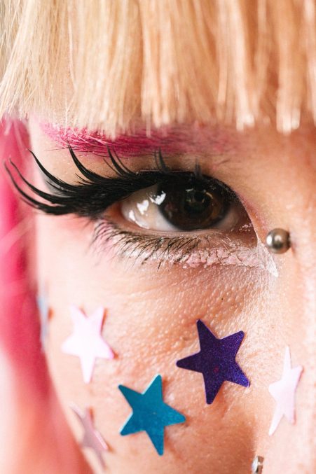 Close-up of a person's eye with colourful star stickers and bold eyelashes, showcasing creative makeup and expressive eye detail.