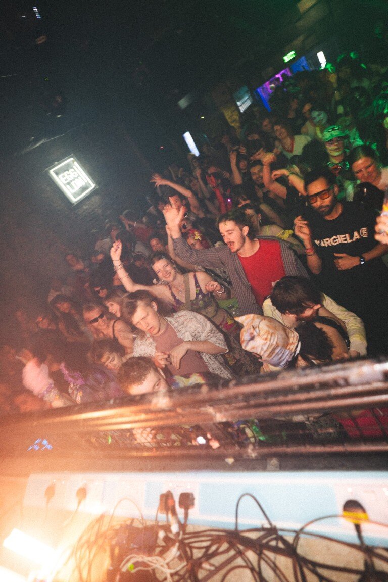 Lively crowd dancing at a DJ club with colourful lights and energetic atmosphere.