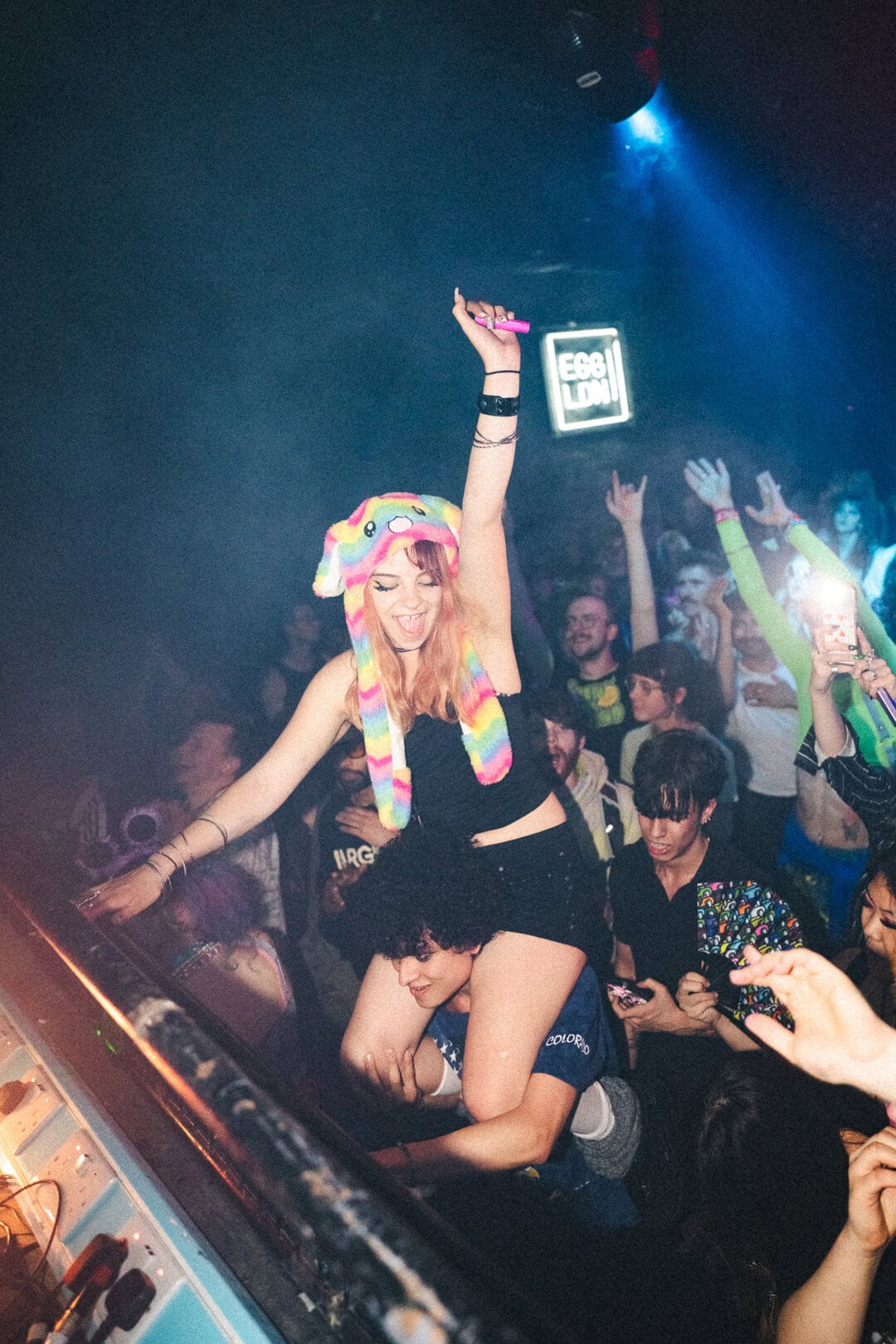 Bright young woman with rainbow hat dancing at lively nightclub event.