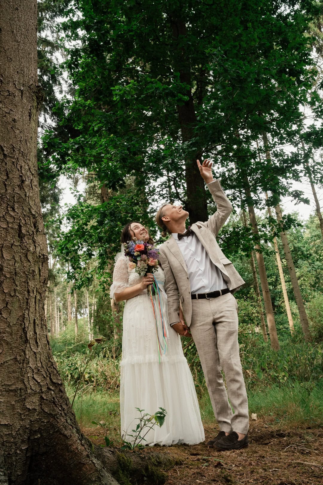 Aerial shot of a happy couple in wedding attire enjoying nature in a forest, celebrating love surrounded by tall trees and green foliage.