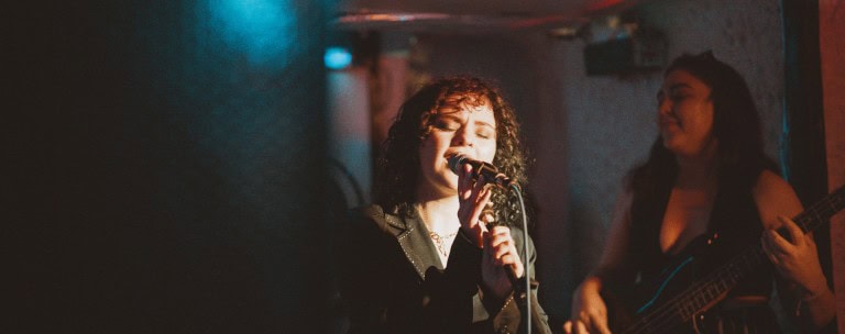Vocalist performing passionately with a guitarist in a dimly lit venue, creating an intimate and energetic live music experience.