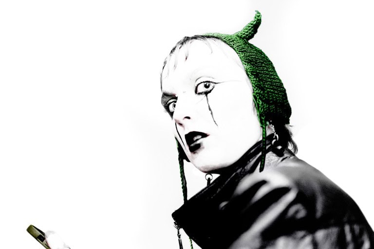 Vivid portrait of a person with striking makeup and surreal elements, wearing a textured green headpiece resembling a hat or accessory.