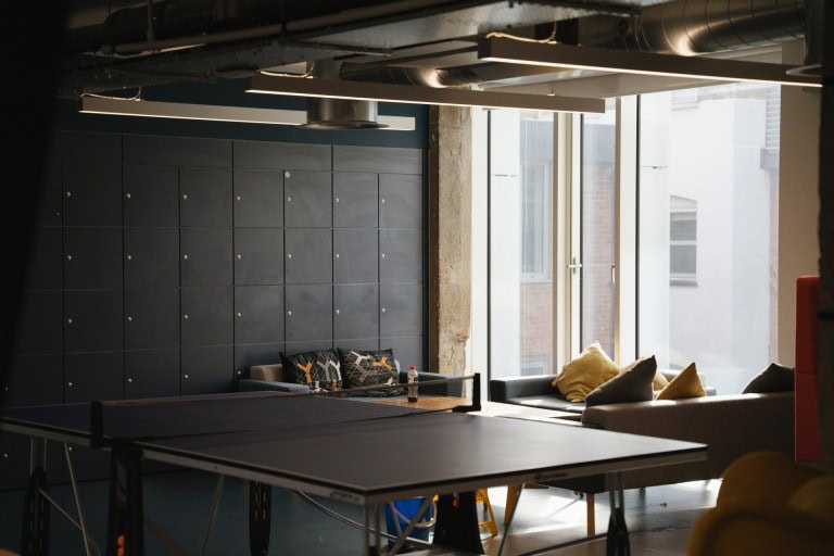 A modern indoor lounge area with large windows, colourful cushions, and a ping pong table in a stylish, contemporary space.