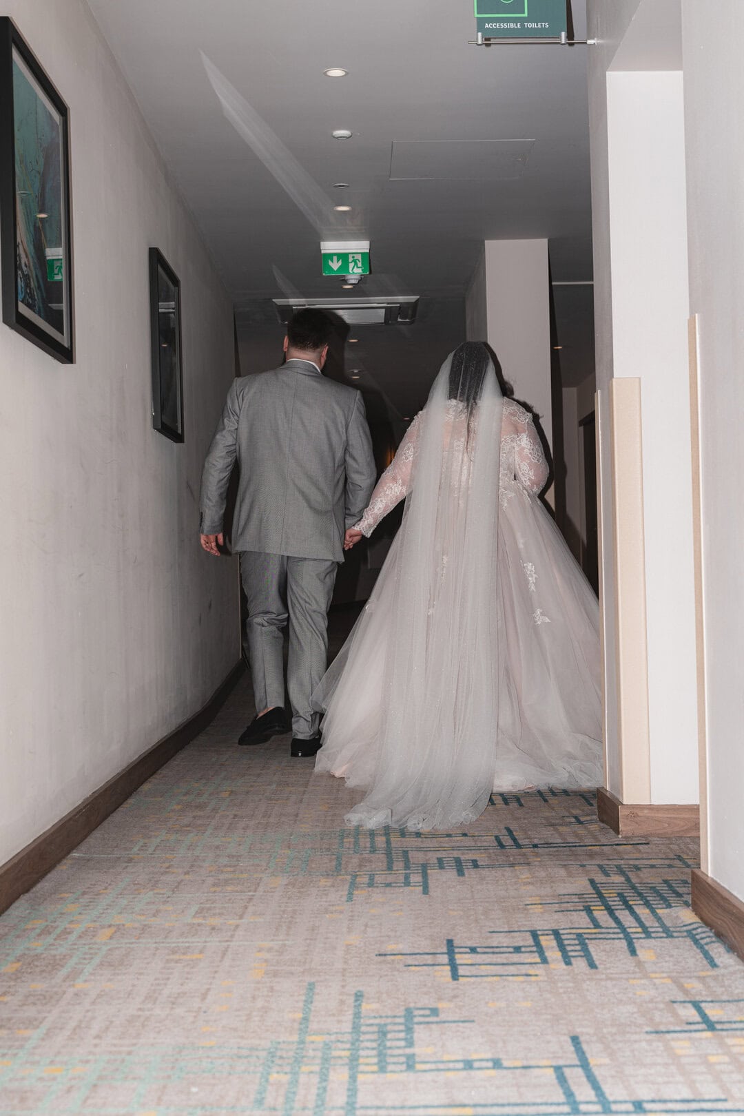 Elegant bride and groom walking hand-in-hand down a corridor after their wedding ceremony.