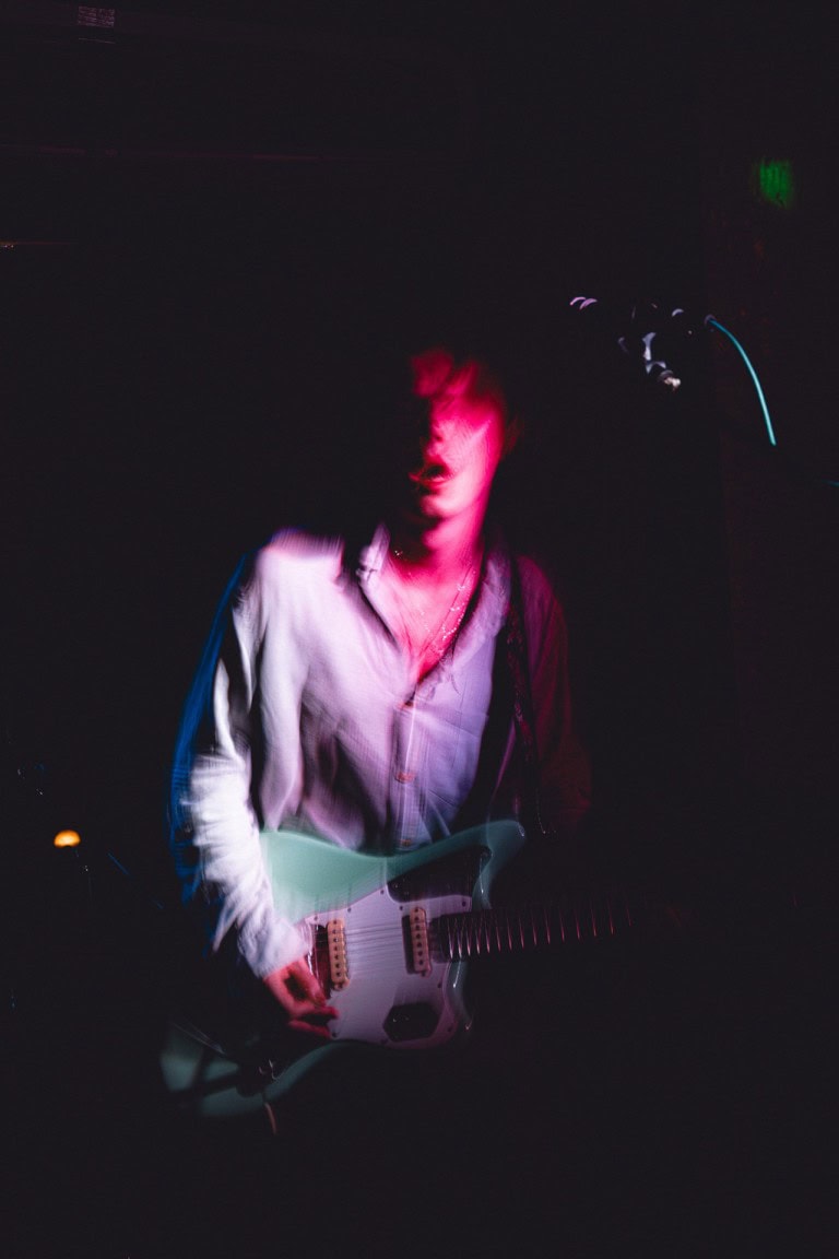 Blurred person playing electric guitar with moody pink and purple lighting, capturing a dynamic and atmospheric performance setting.
