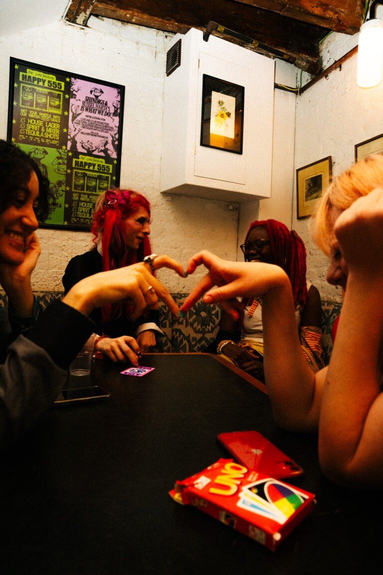 Vibrant social group of friends playing Uno card game in a cosy pub, capturing candid moments, colourful hair, and lively atmosphere for photography portfolio.