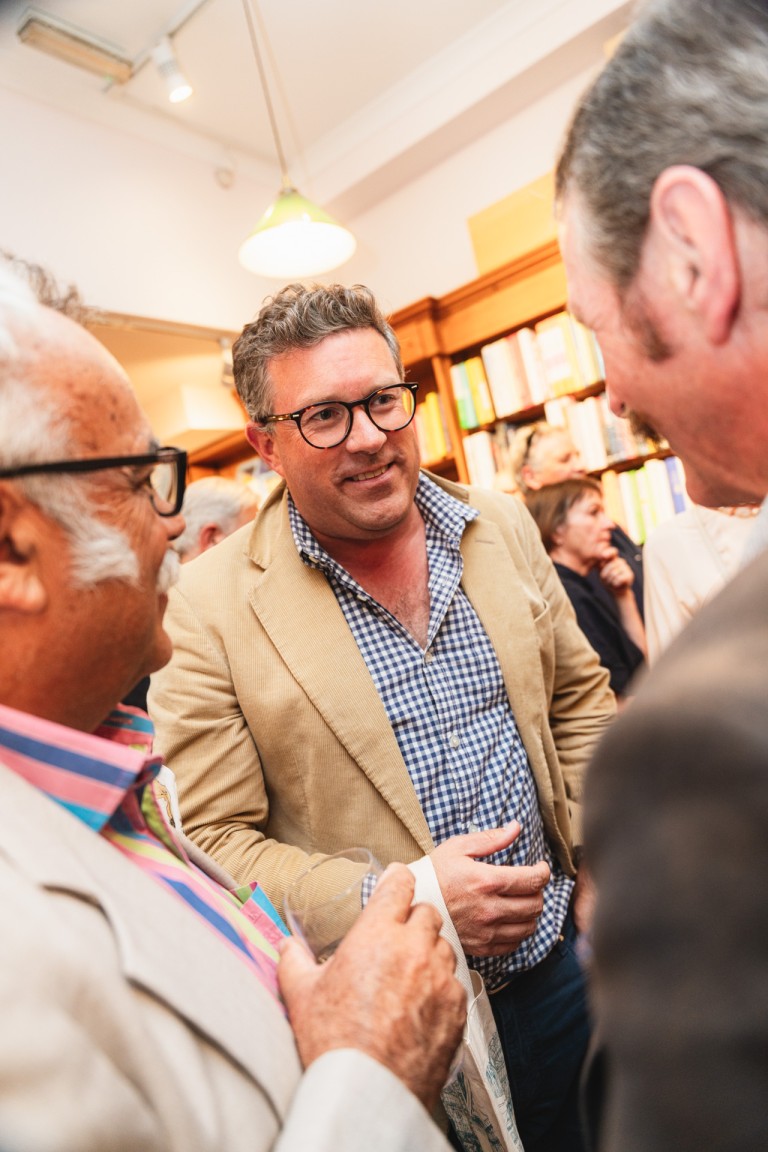 Close-up of a group of people engaged in conversation at a social event in a warmly lit room with bookshelves.