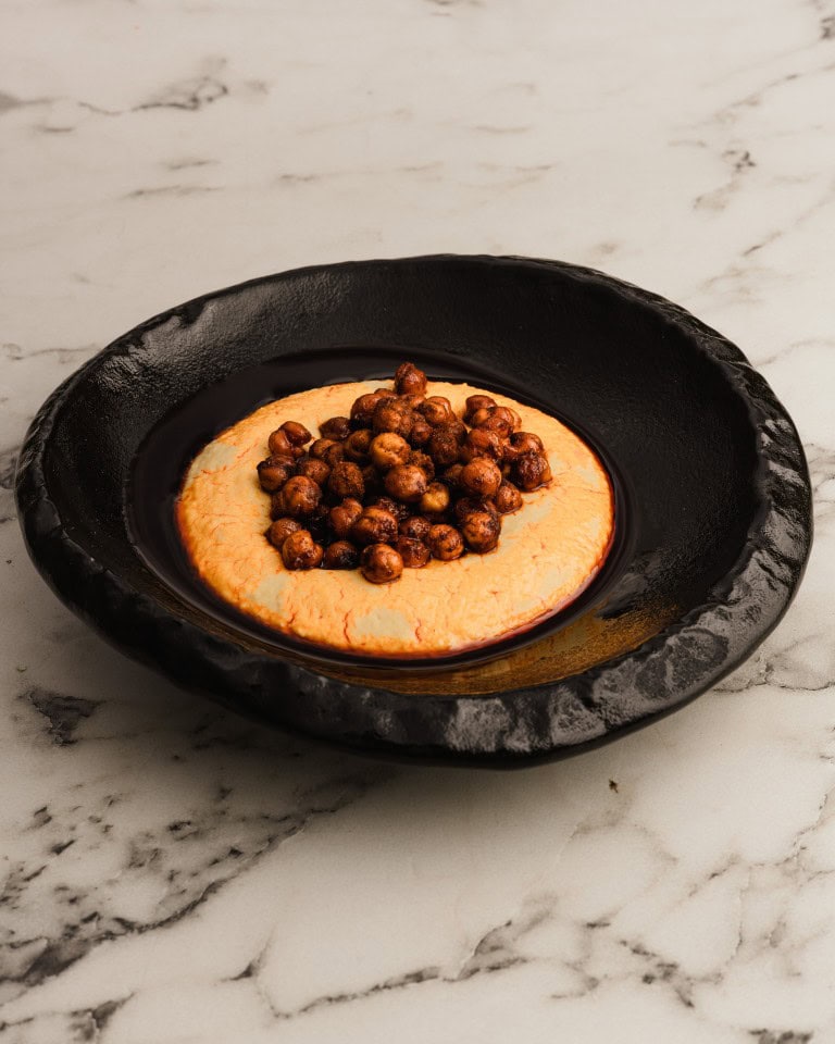 Sweetcorn pancake topped with roasted chickpeas on a dark textured plate against a white marble surface.
