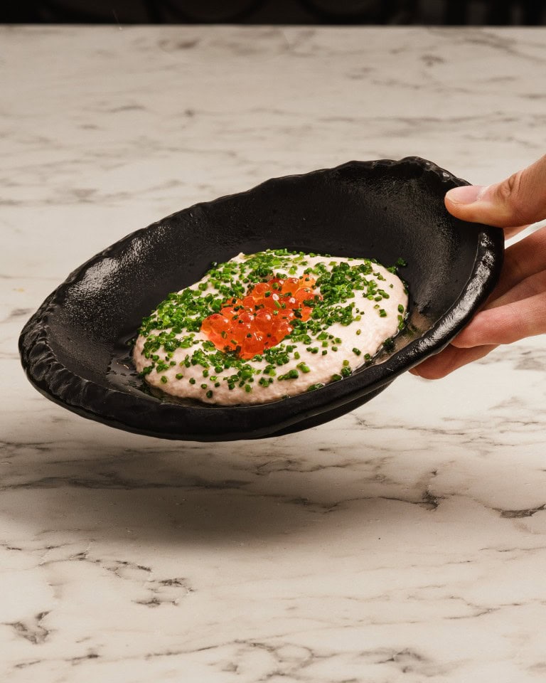 Delicate dish of creamy dip garnished with fresh chopped chives and vibrant red salmon roe, served on a rustic black ceramic plate.