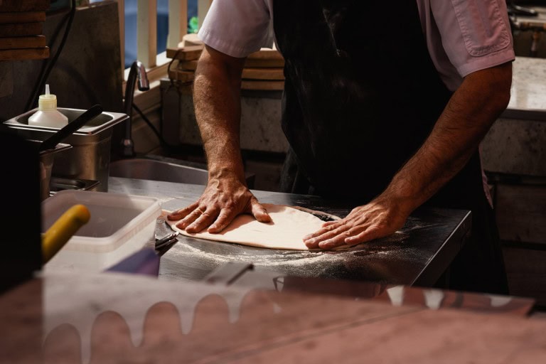 A person preparing dough on a floured surface in a rustic kitchen setting.