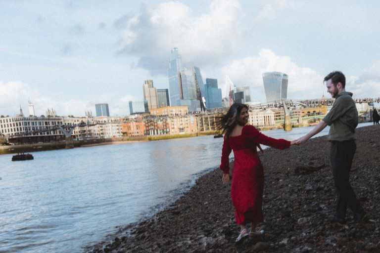 Dancing couple on riverside with modern city skyline in background.