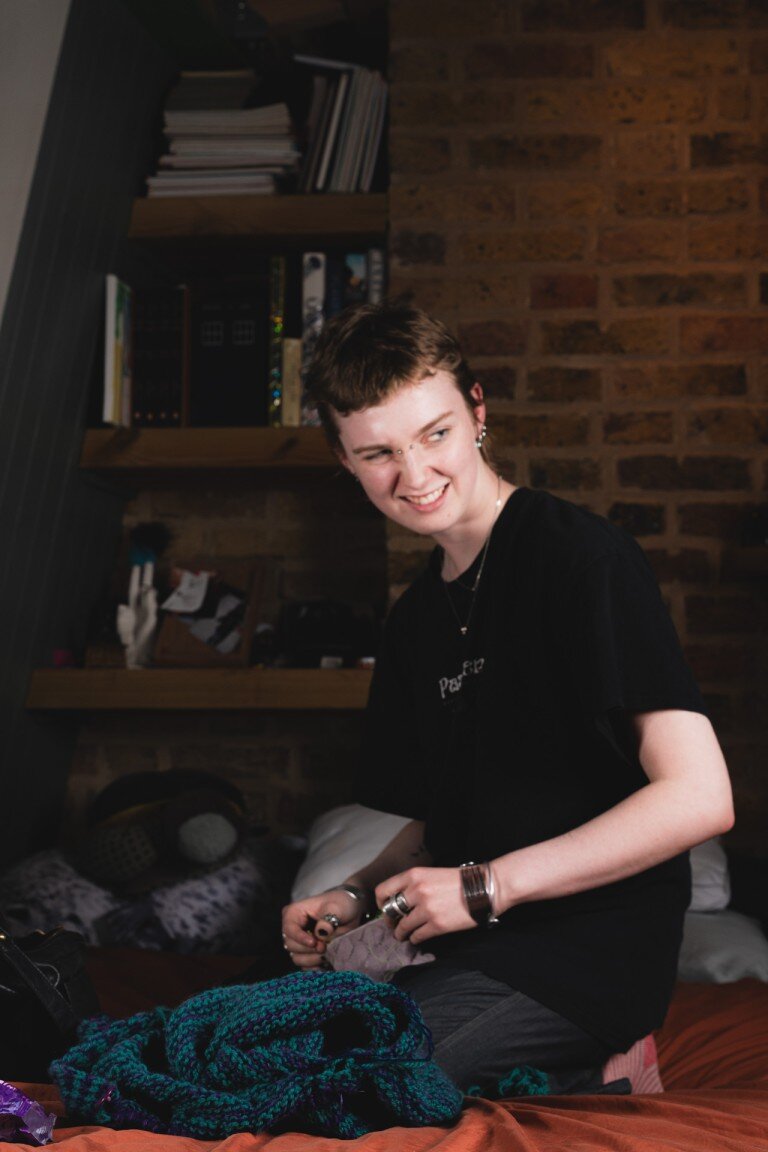 Quirky portrait of a young person with short hair and piercings in a cosy indoor setting, vibrant colours, casual fashion, expressive mood, natural light Photography, Portrait, Lifestyle, Indoor Photography, Young Adults, Creative Portraits, Casual Style, Urban Aesthetic, Warm Lighting, Genuine Expression, Youth Culture, Personal Style, Candid Shot, Contemporary Photography, Personal Expression, Home Environment, Youth Fashion, Lifestyle Photography, Artistic Portrait, Modern Portraiture, Casual Fashion, Warm Atmosphere.