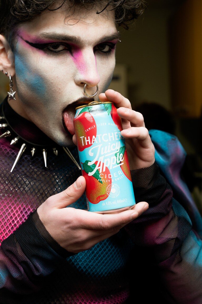 Vibrant makeup and punk-inspired accessories highlight a person engaging with a colourful can of cider. Their bold style and expressive look make a striking impression.