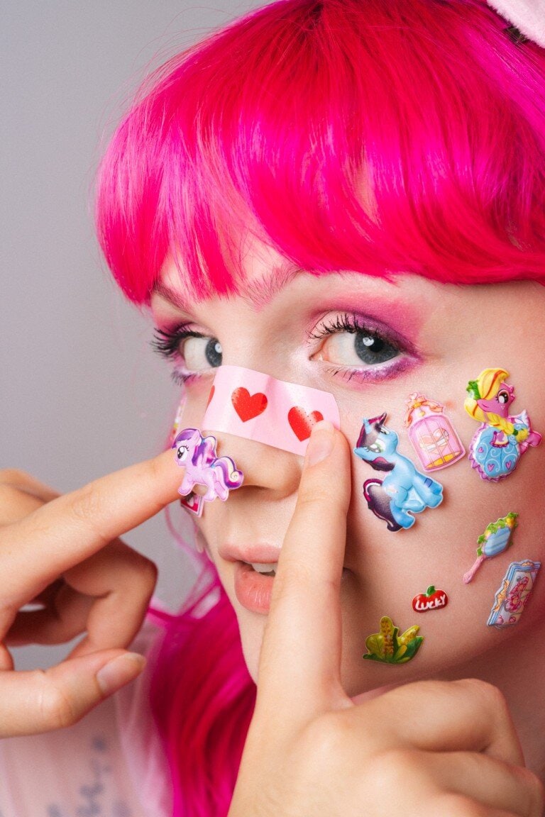 Vibrant portrait of a young woman with bright pink hair and colourful unicorn stickers, showcasing creative fashion and portrait photography.