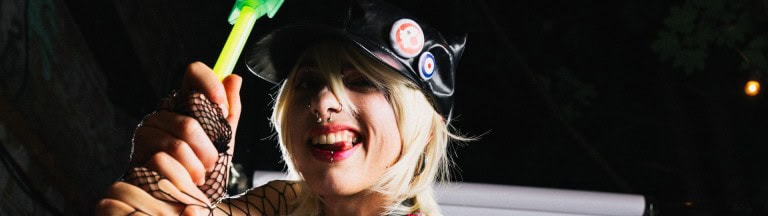 Bright, rebellious woman with blonde hair, playful expression, wearing punk fashion and accessories, capturing candid nightlife photography.