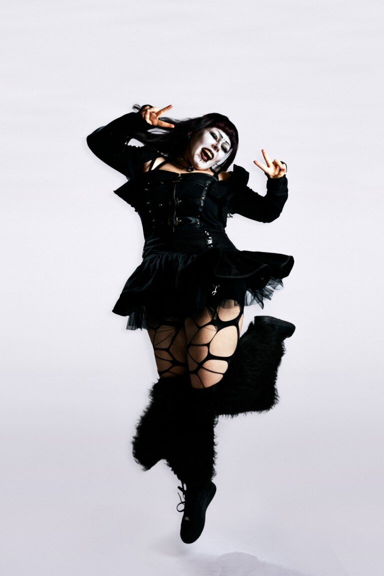 Dynamic goth fashion photoshoot with alternative edgy style, featuring a woman in black clothing, fishnet tights, and furry boots.